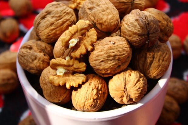 Close up of walnuts in shells and halves in a white bowl with natural textures