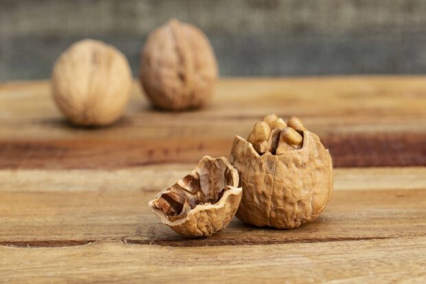 Cracked walnuts with whole walnuts on wooden surface displaying natural walnuts texture