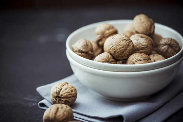 A close up of walnuts in a white bowl on a cloth napkin on a dark surface
