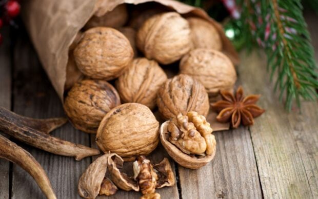 A close up of walnuts in shells and halves on a wooden surface with some spices and greenery