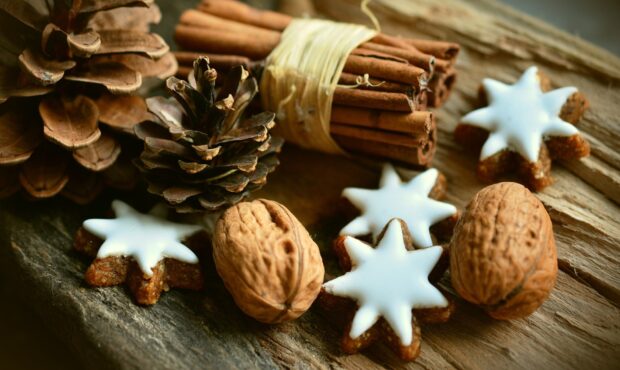 A close up of walnuts with cinnamon sticks and star shaped cookies on a wooden surface