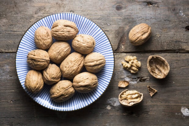 A collection of walnuts in shells on a plate with some cracked walnuts displayed on a wooden surface