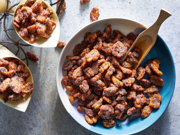 Caramelized walnuts coated with sugar sprinkled in a bowl and wooden trays on a textured surface