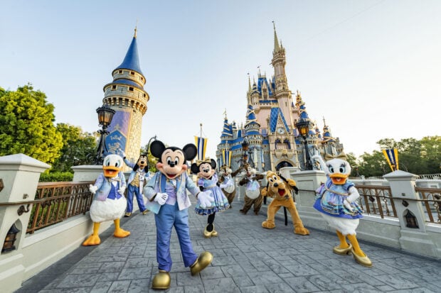 Disney characters dressed in festive outfits walking in front of the Walt Disney World Resort castle