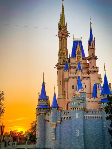 The iconic castle at Walt Disney World Resort is glowing during a vibrant sunset