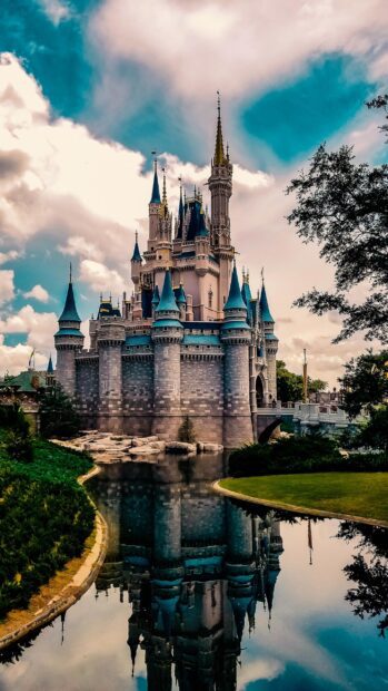 Walt Disney World Resort castle with blue spires reflected in calm water under cloudy sky