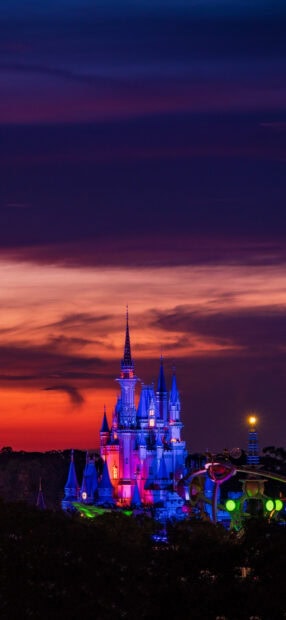 The iconic Walt Disney World Resort castle illuminated at sunset with a colorful sky background