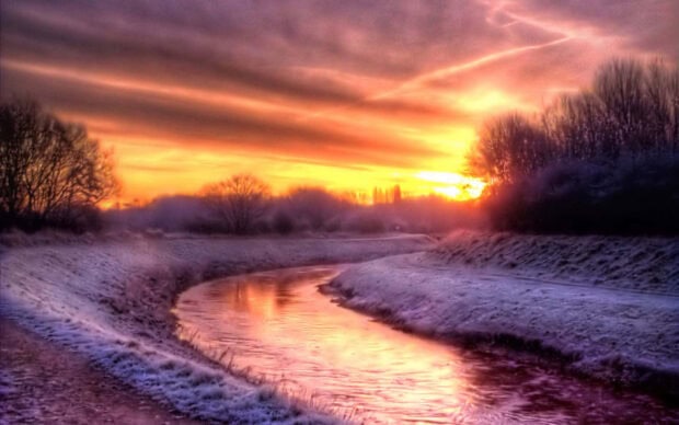 A winter sunset scene with a frosty river surrounded by bare trees and glowing sky