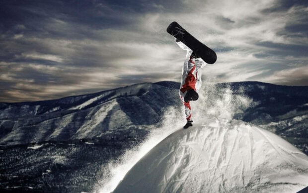 Snowboarder performing a handstand trick on a snowy mountain slope in winter