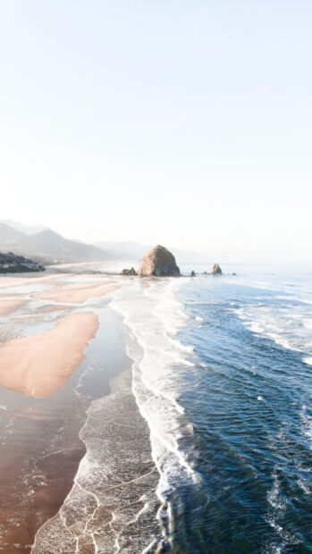 A serene coastal landscape with ocean waves meeting sandy beach and rock formations during summer