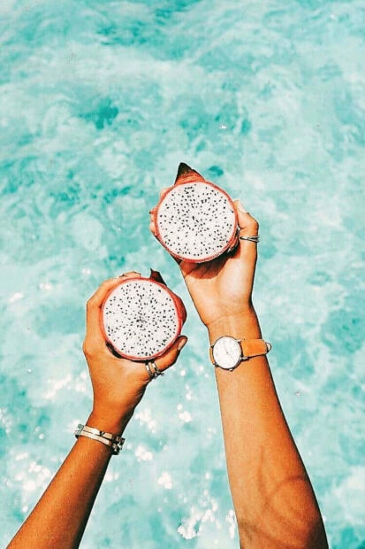 Hands Holding Dragon Fruit Over Clear Blue Water with Summer Vibe