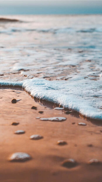 Gentle ocean waves washing over a sandy beach at sunset with warm summer tones