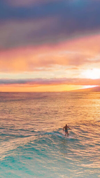 A man surfing on the ocean wave during an atmospheric summer sunset