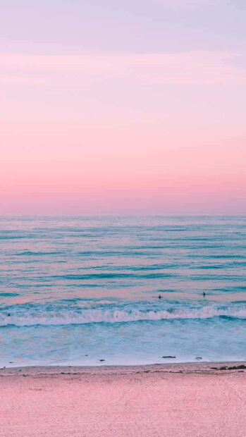 Calm ocean waves under a pastel pink sky at the beach during summer dusk