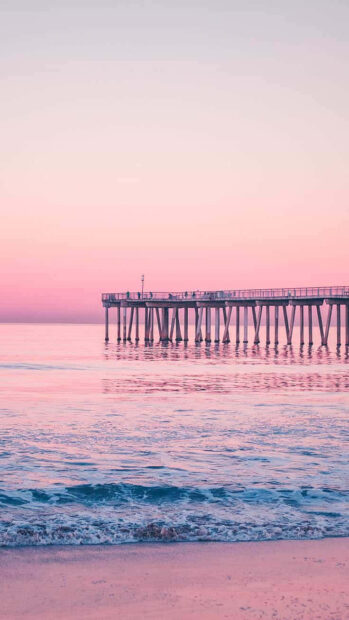 Pink sunset summer pier with gentle ocean waves and clear sky