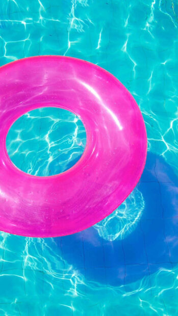 Pink float ring in bright summer pool water with clear blue waves