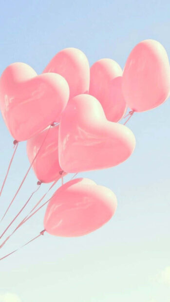 Pink heart shaped balloons floating against a clear blue sky on a pastel summer day