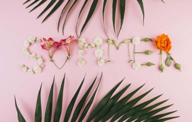 Summer spelled with flowers and green leaves on a pink surface