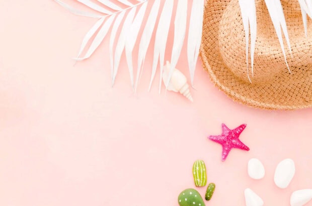 A pink summer scene with a straw hat starfish seashell and painted cactus on a soft pink surface