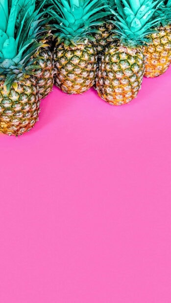 Fresh pineapples arranged on vibrant pink summer surface