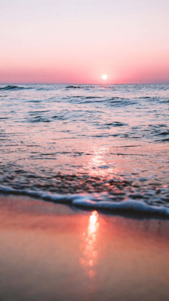 Pink summer sky and ocean surface reflecting sunlight during sunset