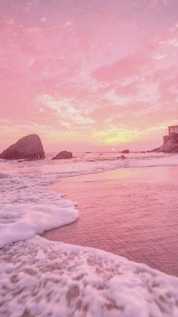 Pink summer sky with ocean waves and rocky shore at sunset