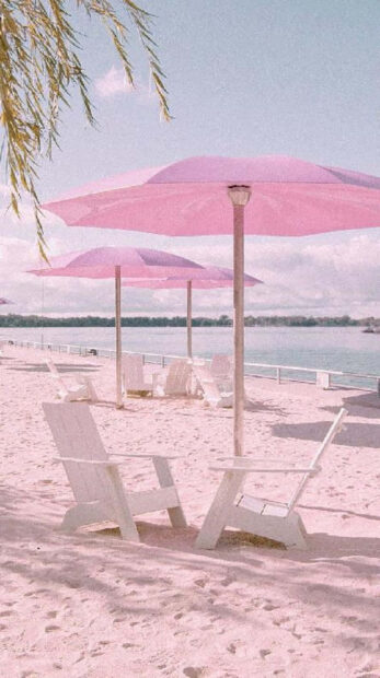 White chairs on pink sand under pink umbrellas at a tranquil summer beach