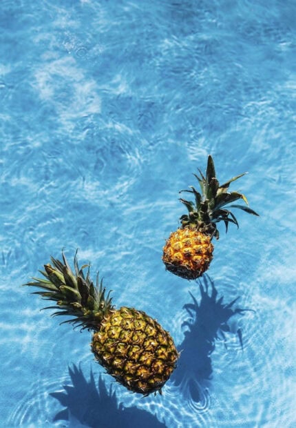Two pineapples floating in clear blue water with summer vibes
