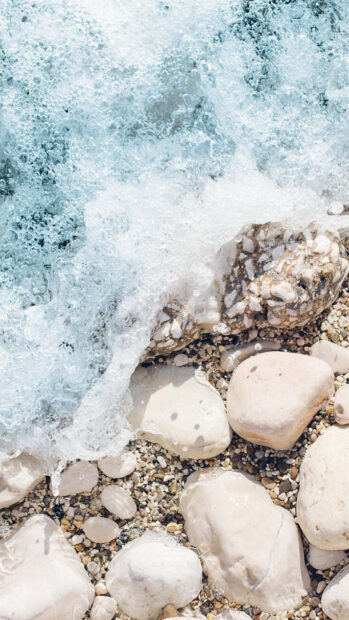 Smooth stones on the beach with gentle waves crashing and foam forming around them