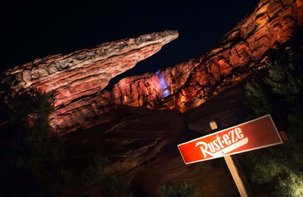 Rust eze sign with illuminated rock formations in Radiator Springs at night