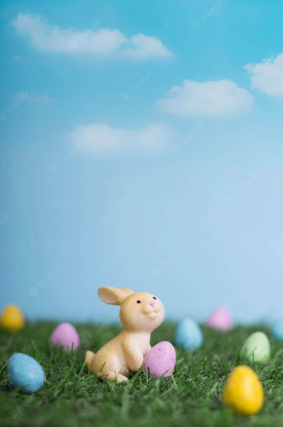 Cute bunny figure holding an Easter egg on green grass in a spring scene