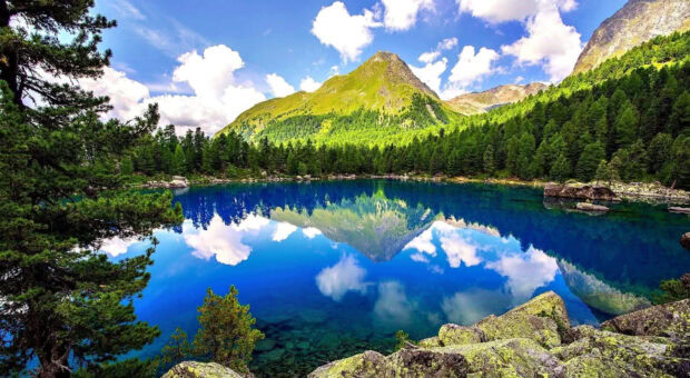 Clear spring mountain landscape with lake reflection and green forest in spring