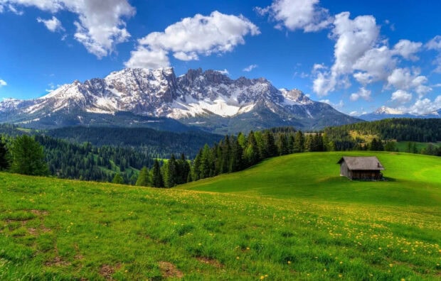 Snow capped mountain range with green spring valley and wooden cabin in the foreground
