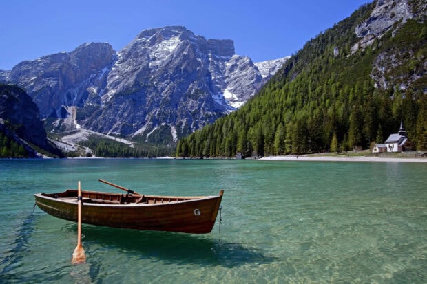 A wooden boat floats on clear water with spring mountain scenery in the background