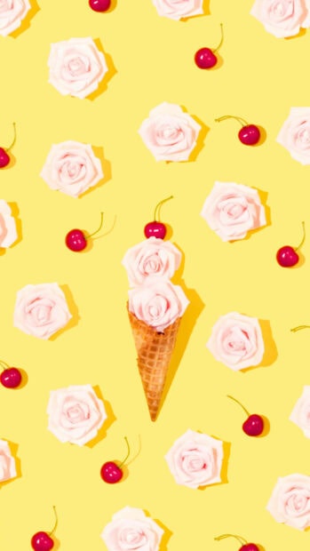 A waffle cone filled with pink roses surrounded by cherries on a bright yellow surface
