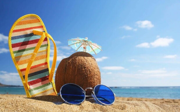 A colorful striped sandal with a coconut and blue sunglasses on sandy beach