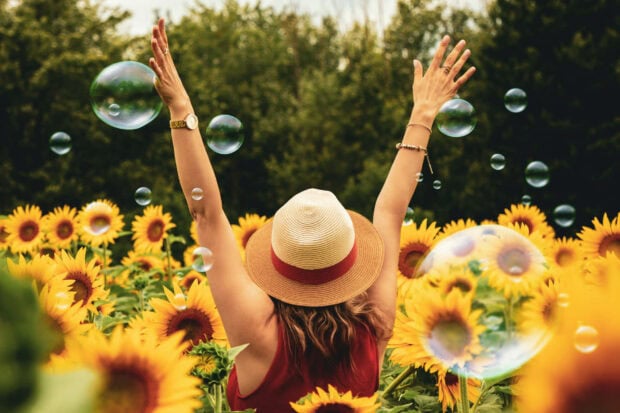 A woman wearing a sunhat enjoying a sunflower field with bubbles floating around