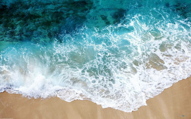 Aerial view of ocean waves crashing against a sandy shore during summer