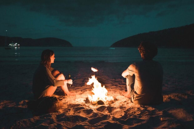 Two people enjoying summer campfire on the beach at night