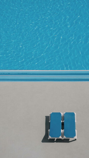 Two empty blue lounge chairs near a calm poolside on a sunny summer day