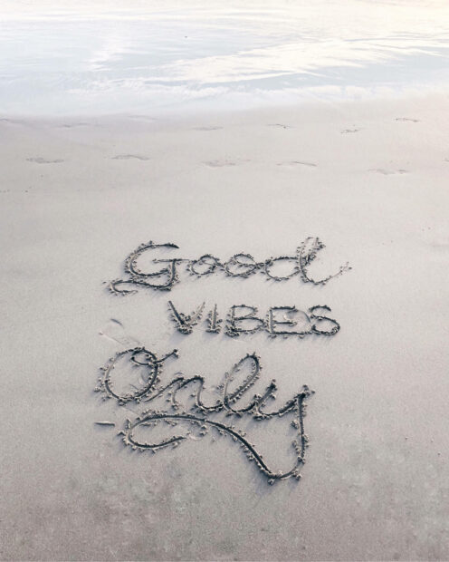 Good vibes and salty words written in the sand on a beach