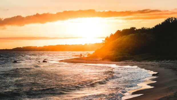 A peaceful summer sunset along the coast with waves and a person walking near the shore