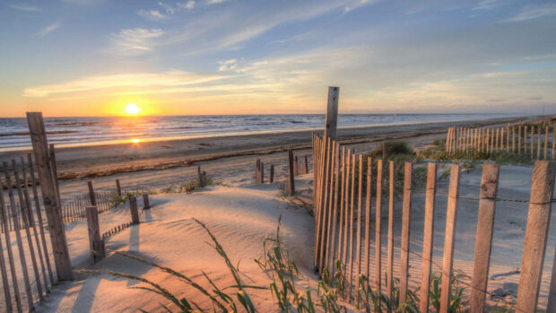 A serene summer vibes scene of sandy dunes and wooden fences by the beach at sunset