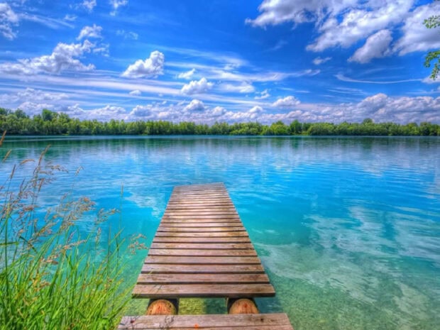 A wooden pier extending over clear summer water surrounded by peaceful nature