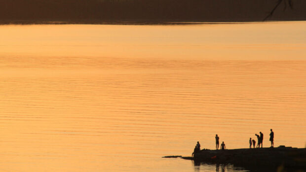 Silhouettes of people enjoying summer moments at the lake shore during sunset
