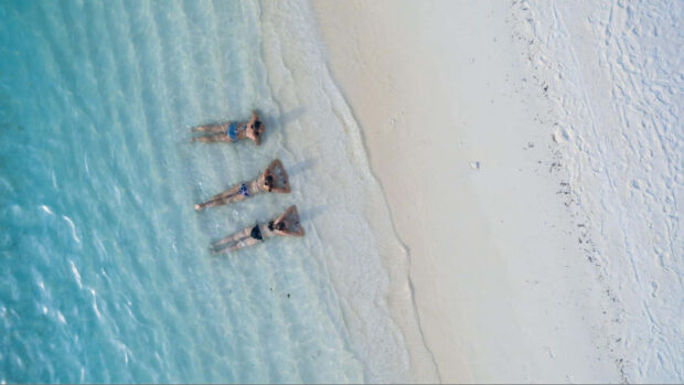 Three people relaxing in clear water near the beach during summer vibes