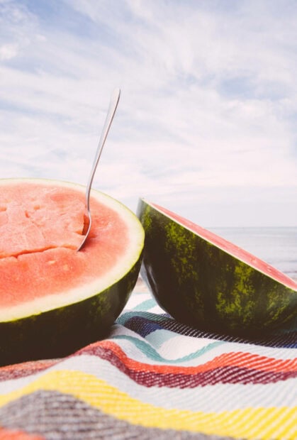 Fresh watermelon slice on colorful blanket under blue sky