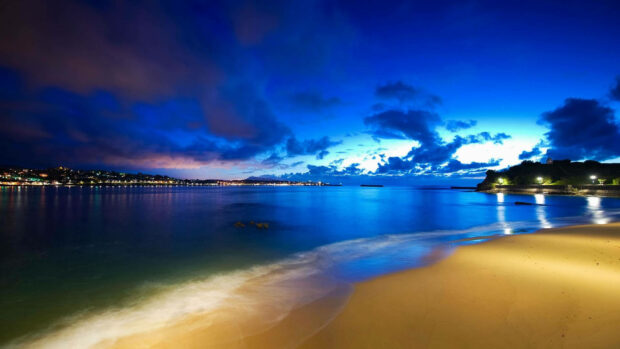 A summer beach landscape with calm sea and glowing city lights at dusk