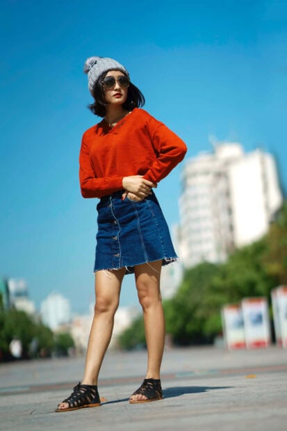 Young woman wearing sweater and denim skirt standing outdoors on a sunny day