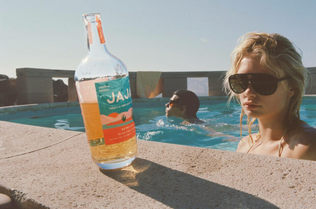 A bottle of tequila beside a woman and a man enjoying a pool on a summer day